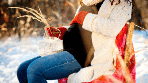 A cozy traveler wearing a white coat and red gloves sitting in the snow, capturing relaxing winter travel bucket list ideas.