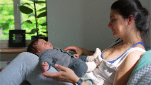 A mother using responsive parenting styles while looking affectionately at her newborn baby resting on her lap in a brightly lit room.