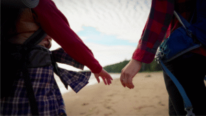 Close-up of two people in a healthy relationship reaching out to hold hands while walking outdoors.